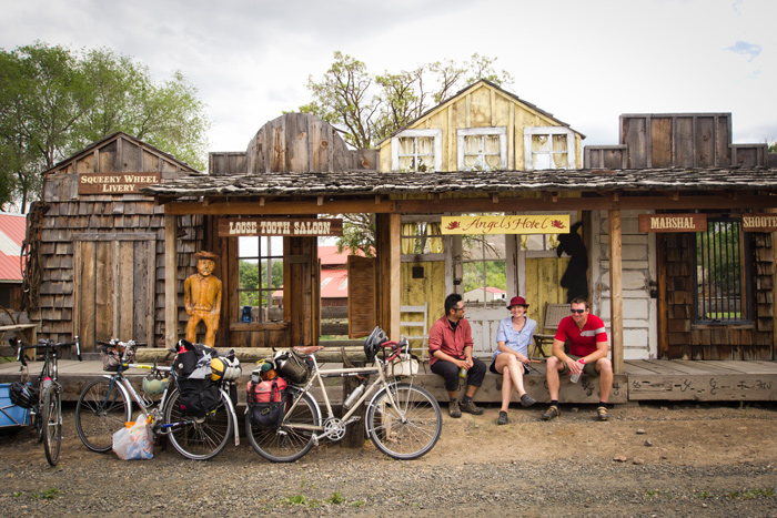 Three people sit the stoop of the Angel's Hotel next to the Loose Tooth Saloon.